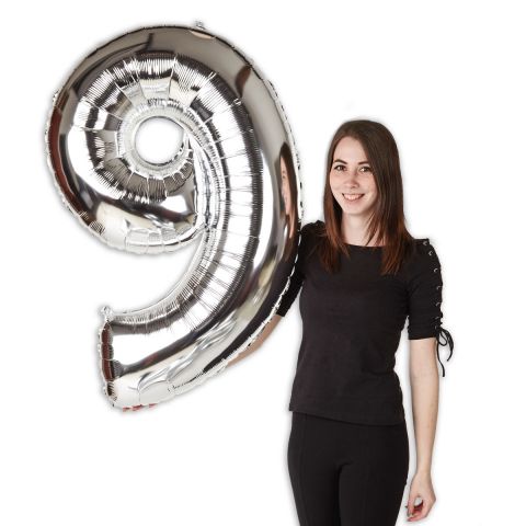 Großer Folienballon, Zahl "9" in Silber, im Größenverhältnis zu einer Person zu sehen.